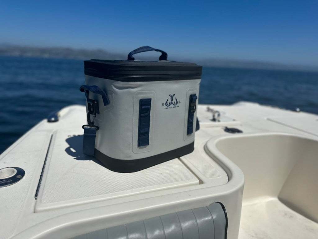 A large cooler bag on a fishing boat at sunrise, surrounded by fishing gear and scenic nature with mountains and trees in the background.