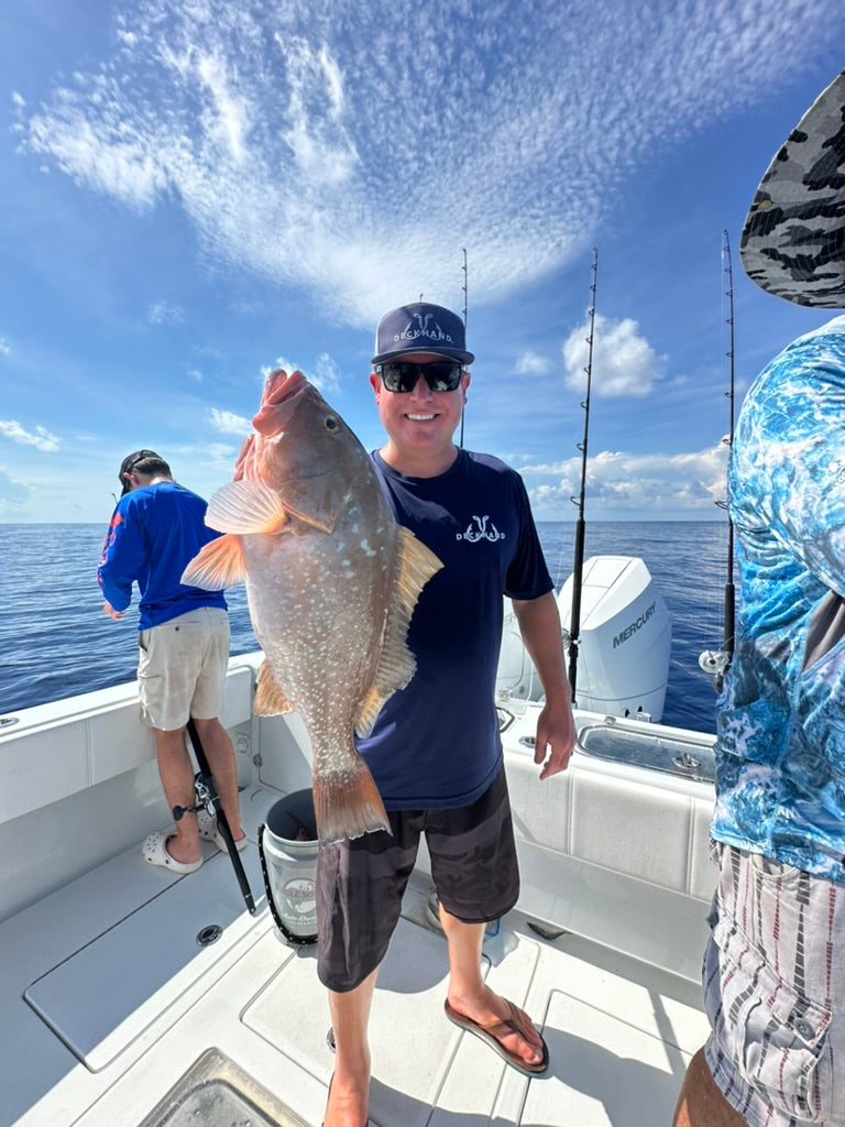 Confident angler wearing a visor hat fishing on a boat with Deckhand Sports gear on a sunny day.